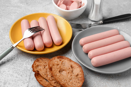 Bowl and plates with tasty thin sausages on gray backgroundの写真素材