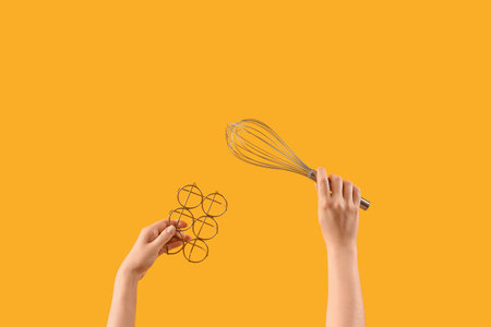 Female hands holding whisk and egg holder on yellow backgroundの写真素材