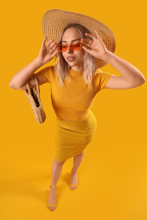 Young woman in stylish sunglasses with bag on orange backgroundの写真素材