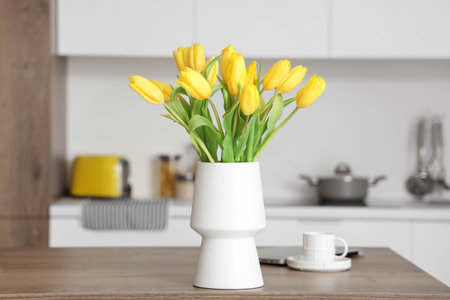 Vase with yellow tulip flowers on wooden table in modern kitchenの写真素材