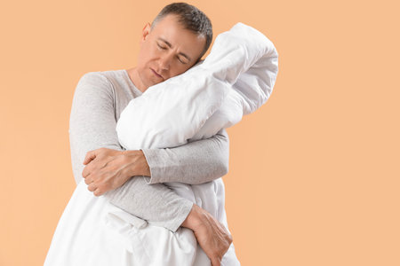 Mature man with soft blanket sleeping on beige backgroundの写真素材