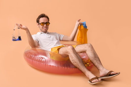 Young man with snorkeling mask, flippers and inflatable ring lying on beige backgroundの写真素材