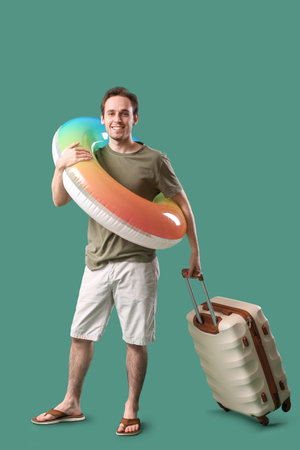 Young man with inflatable ring and suitcase on green backgroundの写真素材