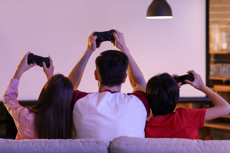Father with his little children playing video game at home in the evening, back view