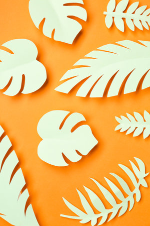 Light paper tropical leaves on orange backgroundの写真素材
