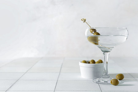 Glass of tasty martini and olives on white tile tableの写真素材