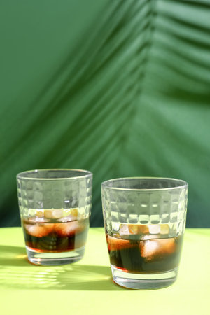 Glasses of rum with ice cubes on green background
