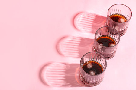 Glasses of rum with ice cubes on pink background