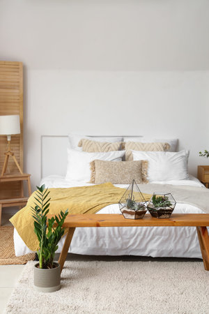 Interior of light bedroom with bed, florariums and bench