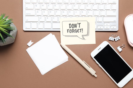 Reminder with stationery, mobile phone and computer keyboard on brown backgroundの写真素材