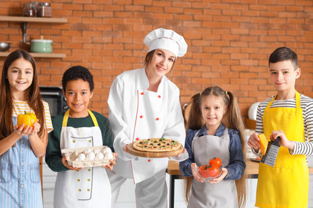Female chef with prepared pizza and group of little children after cooking class in kitchenの写真素材