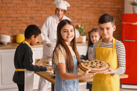 Little children with prepared pizza after cooking class in kitchenの写真素材