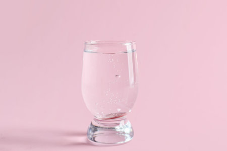 Glass of water with soluble tablet on pink background