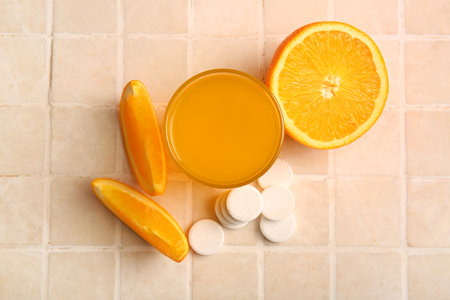 Glass of vitamin C effervescent tablet dissolved in water and orange on tiled tableの写真素材