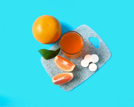 Board with glass of vitamin C effervescent tablet dissolved in water and grapefruit on blue backgroundの写真素材
