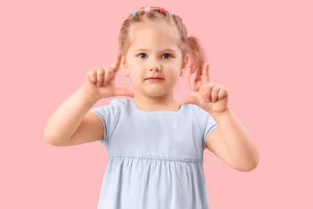 Funny little girl showing loser gesture on pink backgroundの写真素材