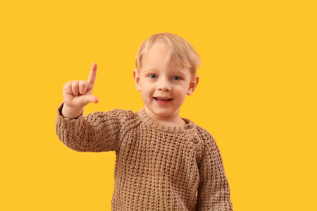 Funny little boy showing loser gesture on yellow backgroundの写真素材