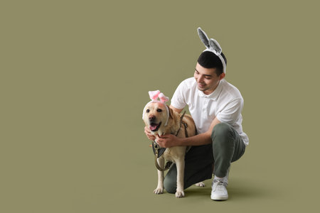 Young man and cute Labrador dog in bunny ears on green background