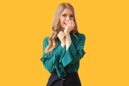 Happy young woman biting nails on yellow background