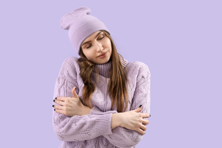Pretty young woman in knitted sweater and hat on lilac background