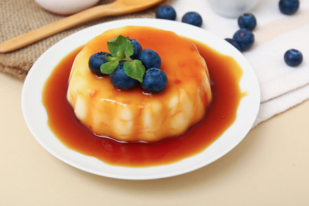 Plate with delicious pudding, blueberries and mint covered by caramel syrup on beige backgroundの写真素材