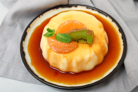 Plate with delicious pudding, kiwi and tangerines covered by caramel syrup on gray backgroundの写真素材