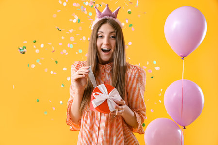 Surprised young woman with birthday gift on yellow backgroundの写真素材