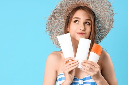 Young woman with bottles of sunscreen cream on blue background, closeup