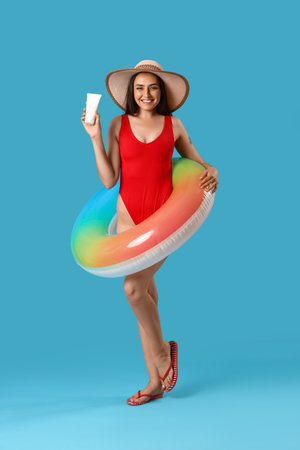 Young woman with sunscreen cream and inflatable ring on blue backgroundの写真素材