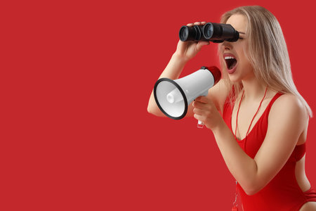 Female lifeguard with binoculars shouting into megaphone on red backgroundの写真素材