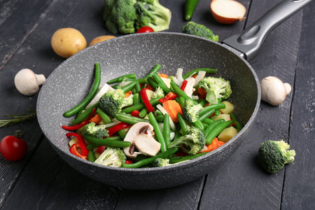 Frying pan with fresh vegetables on black wooden backgroundの写真素材