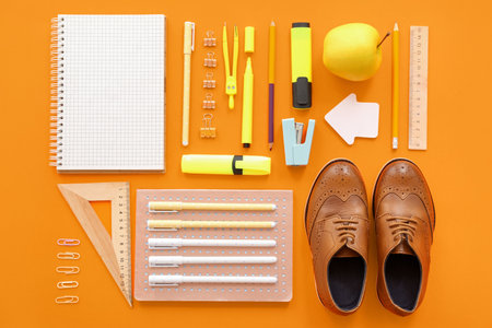 Cute shoes with fresh apple and different stationery on orange backgroundの写真素材