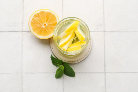 Glass of infused water with lemon and mint on white tile tableの写真素材