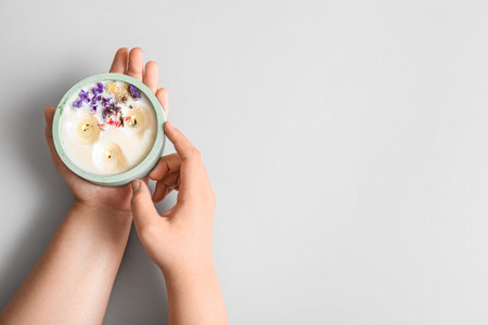 Female hands with burning candle and flowers on gray backgroundの写真素材
