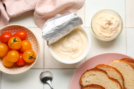 Plastic container and bowl of tasty cream cheese and tomatoes on white tile backgroundの写真素材