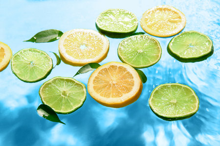 Slices of fresh lemon and lime in water on blue backgroundの写真素材