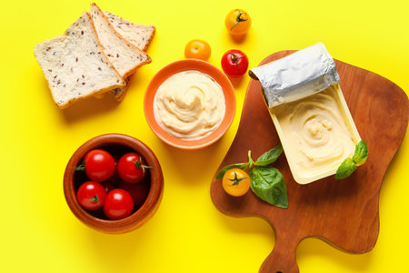 Plastic container and bowl of tasty cream cheese with tomatoes on yellow backgroundの写真素材