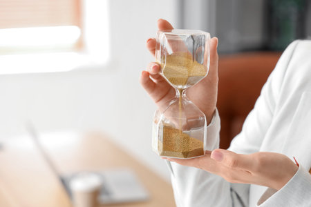 Young businesswoman with hourglass in office, closeup