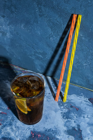 Glass of cold Cuba Libre cocktail on blue background