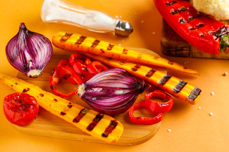 Board with grilled vegetables on orange background