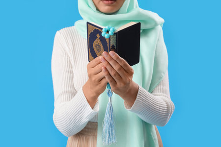 Young Muslim woman with Koran and prayer beads on blue background, closeup. islamic new year...