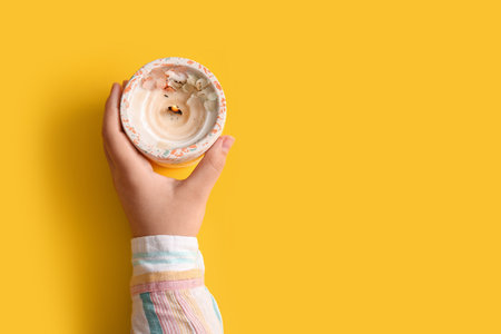 Female hand with burning candle and flowers on yellow backgroundの写真素材