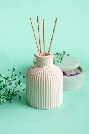 Floral reed diffuser and gypsophila flowers on turquoise background, closeup