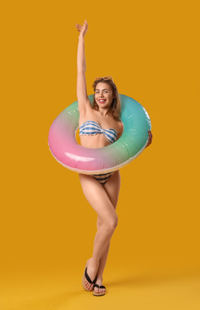 Young woman in swimsuit with inflatable ring on yellow backgroundの写真素材