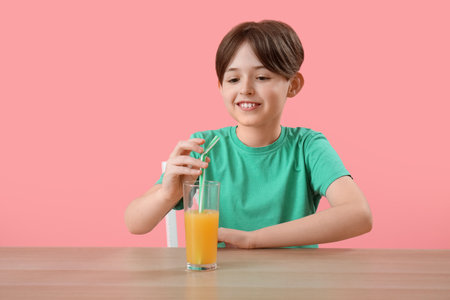 Little boy with glass of orange juice at table on pink backgroundの写真素材