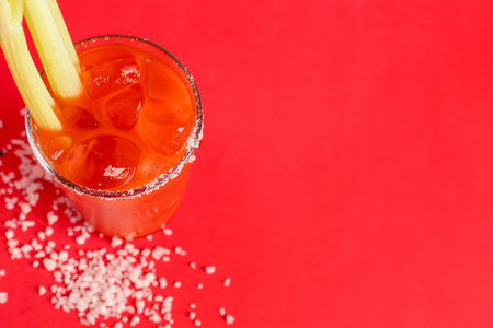 Glass of bloody mary with celery and salt on red backgroundの写真素材