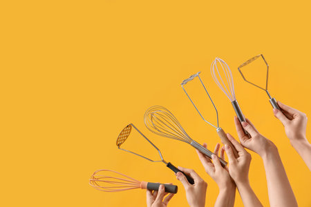 Female hands holding different whisks and mashers on yellow backgroundの写真素材