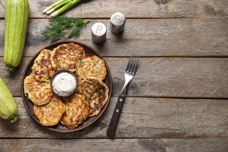 Plate of tasty zucchini fritters with sour cream on wooden backgroundの写真素材