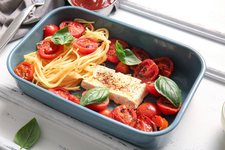 Baking dish of tasty pasta with tomatoes and feta cheese on white wooden backgroundの写真素材
