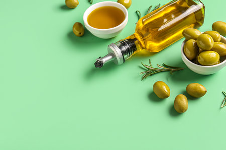 Ripe olives, bowls and bottle of oil on green backgroundの写真素材
